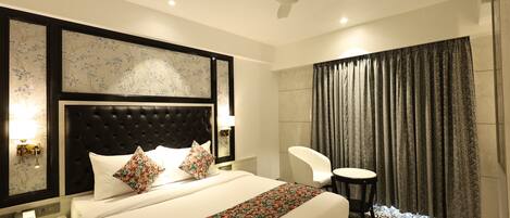 A hotel room with a bed, a desk, a chair, a ceiling fan, and a window with curtains.