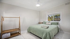 A bedroom with a bed, a wooden wardrobe, a window with a view, and a ceiling fan. - Sea Mist Upstairs Residence (WOOLI)
