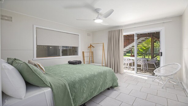 Quarto com cama, ventilador de teto, janela e vista para um pátio externo com cadeiras.