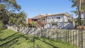 Uma casa de dois andares com deck de madeira e quintal cercado.