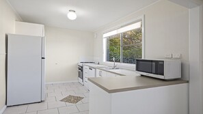 A compact kitchen with white appliances, a window with a view of greenery, and a stone-patterned floor.