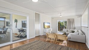 Amplia sala de estar con puerta de vidrio corrediza a un balcón, comedor con mesa y sillas, sofá y televisor en la pared.