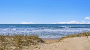 Ein Strand mit Wellen, Sand und vereinzelter Vegetation.