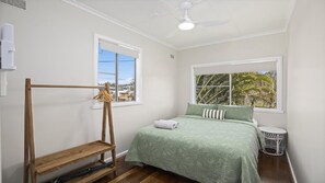 Ein Schlafzimmer mit einem Bett, einer hölzernen Bank, einem Deckenventilator und einem Fenster mit Blick auf Palmen.