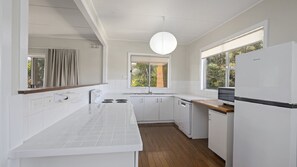 A modern kitchen with white cabinetry, a wooden countertop, a built-in dishwasher, and a window providing natural light.