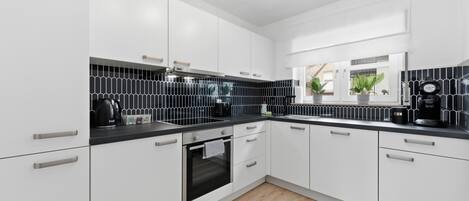 A modern kitchen with white cabinets, black countertops, a built-in oven, and a black backsplash.
