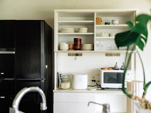 Une cuisine avec un réfrigérateur noir, des placards blancs, un four à micro-ondes et une plante.