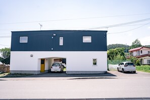 Kaksikerroksinen rakennus, jossa on autotalliin johtava sisäänkäynti, pieni ikkuna ylemmässä kerroksessa ja näkyvä antenni katolla.