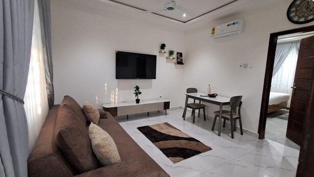 A modern living room with a sofa, TV, dining table, chairs, and a small kitchen area.
