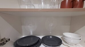 A kitchen shelf with stacked black plates, a white bowl, and a red mug.