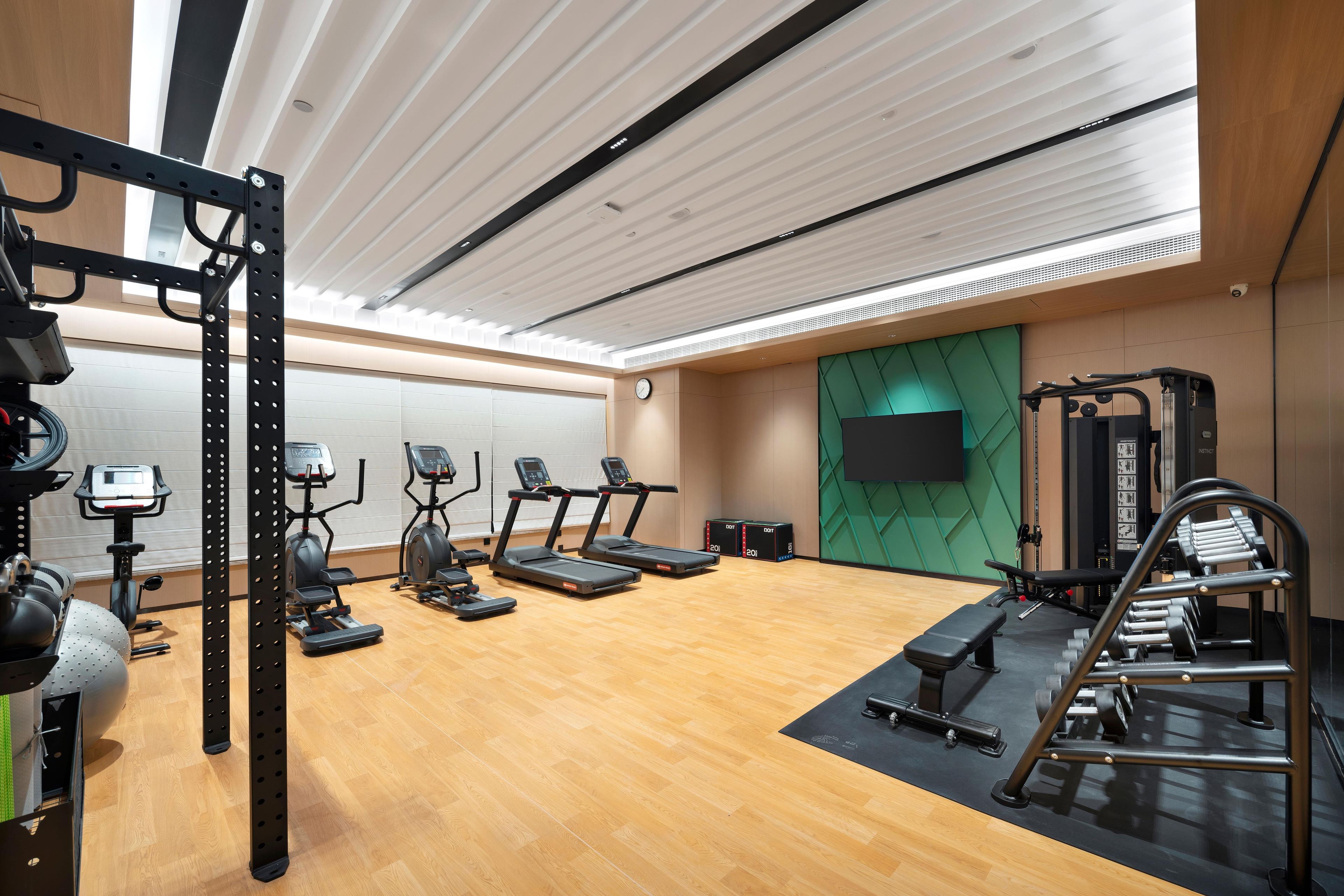 Un gimnasio moderno con cintas de correr, elípticas, una estructura para sentadillas y bancos de pesas.