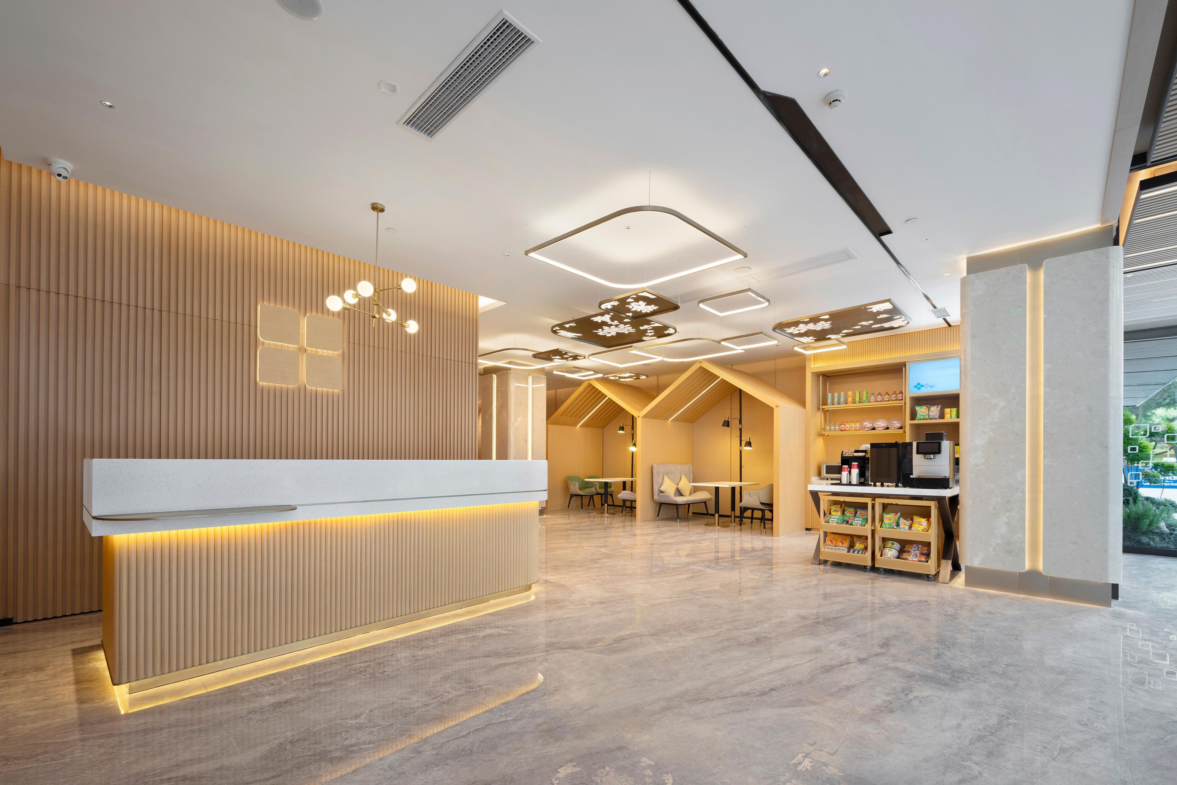 Una moderna zona de recepción con un mostrador de madera, un espacio de espera con mesas y sillas, y una exhibición de aperitivos.