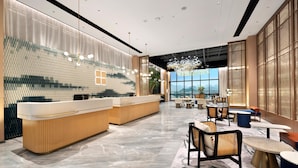 Een moderne hotel lobby met een receptiebalie, zithoek en grote ramen met uitzicht.