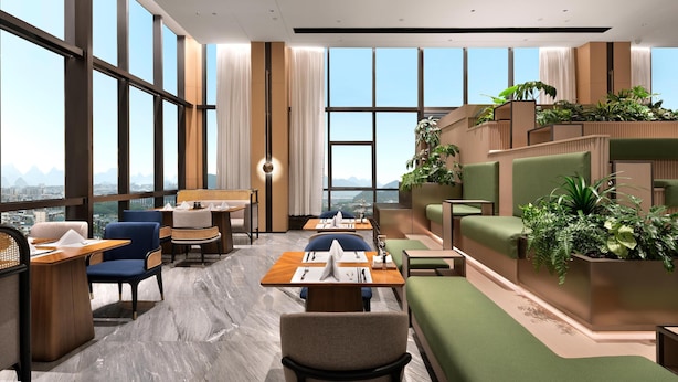 Een moderne hotel lobby met grote ramen, zithoeken en een groene wand van planten.