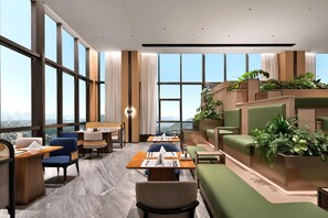 Eine moderne Hotelhalle mit großen Fenstern, Sitzbereichen und einer grünen Pflanzenwand.