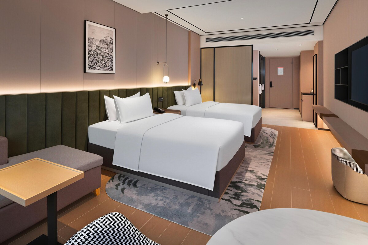 Ett modernt hotellrum med två sängar, en soffa, en TV och ett skrivbord.