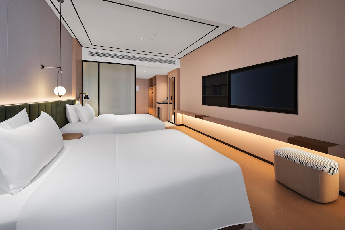 Ett modernt hotellrum med en stor säng, en tv som är monterad på väggen och en liten sittgrupp.