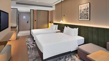 A hotel room with two beds, a sofa, a small table, a TV, and a framed artwork on the wall.