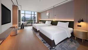 Een moderne hotelkamer met twee bedden, een televisie, een bureau en een groot raam met uitzicht op de stad.