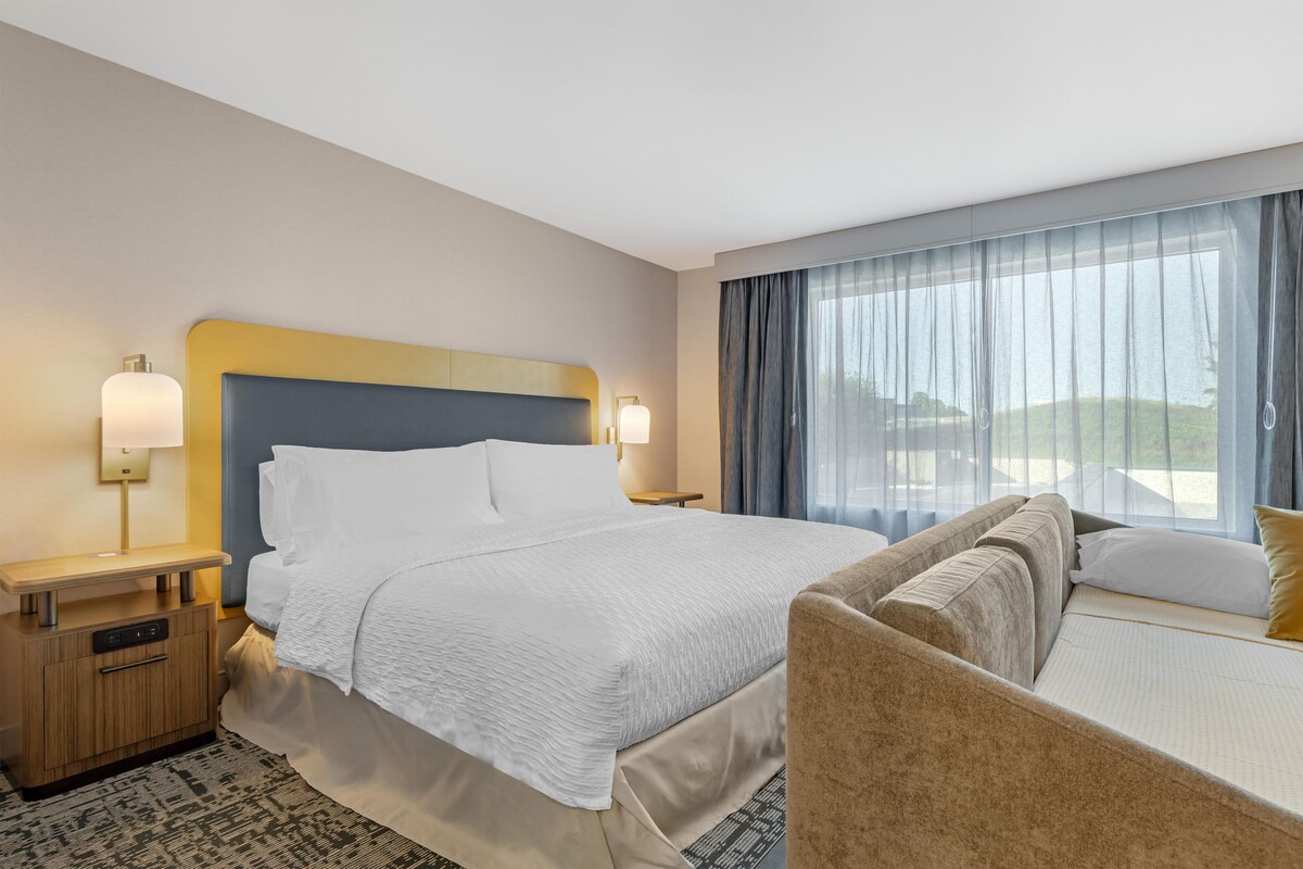 A hotel room with a bed, bedside tables, a desk, and a sofa.