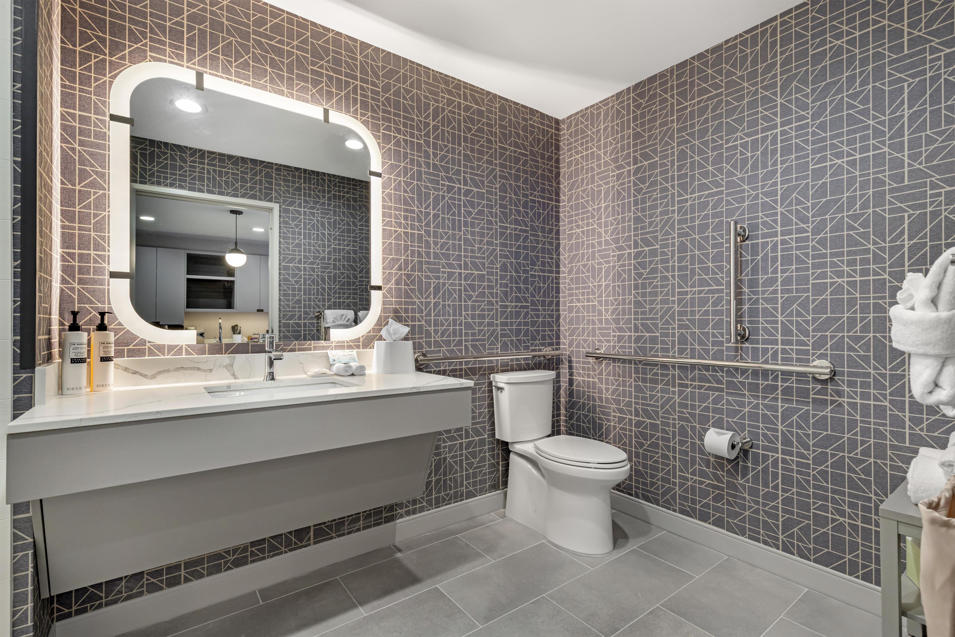A modern bathroom with a vanity, toilet, and a large mirror with lights.