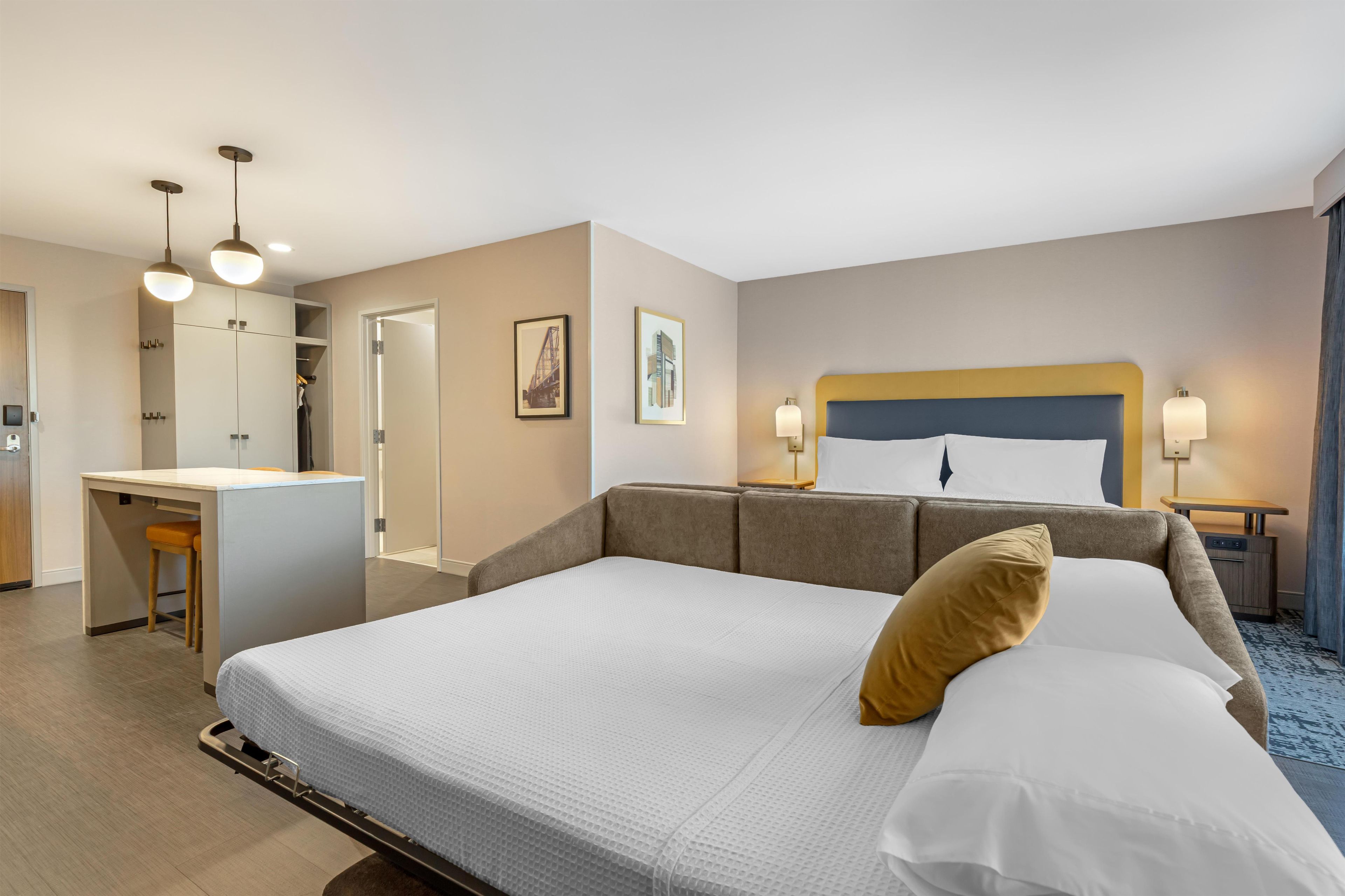Een hotelkamer met een groot bed, een bureau en een stoel. Twee ingelijste foto’s hangen aan de muur.