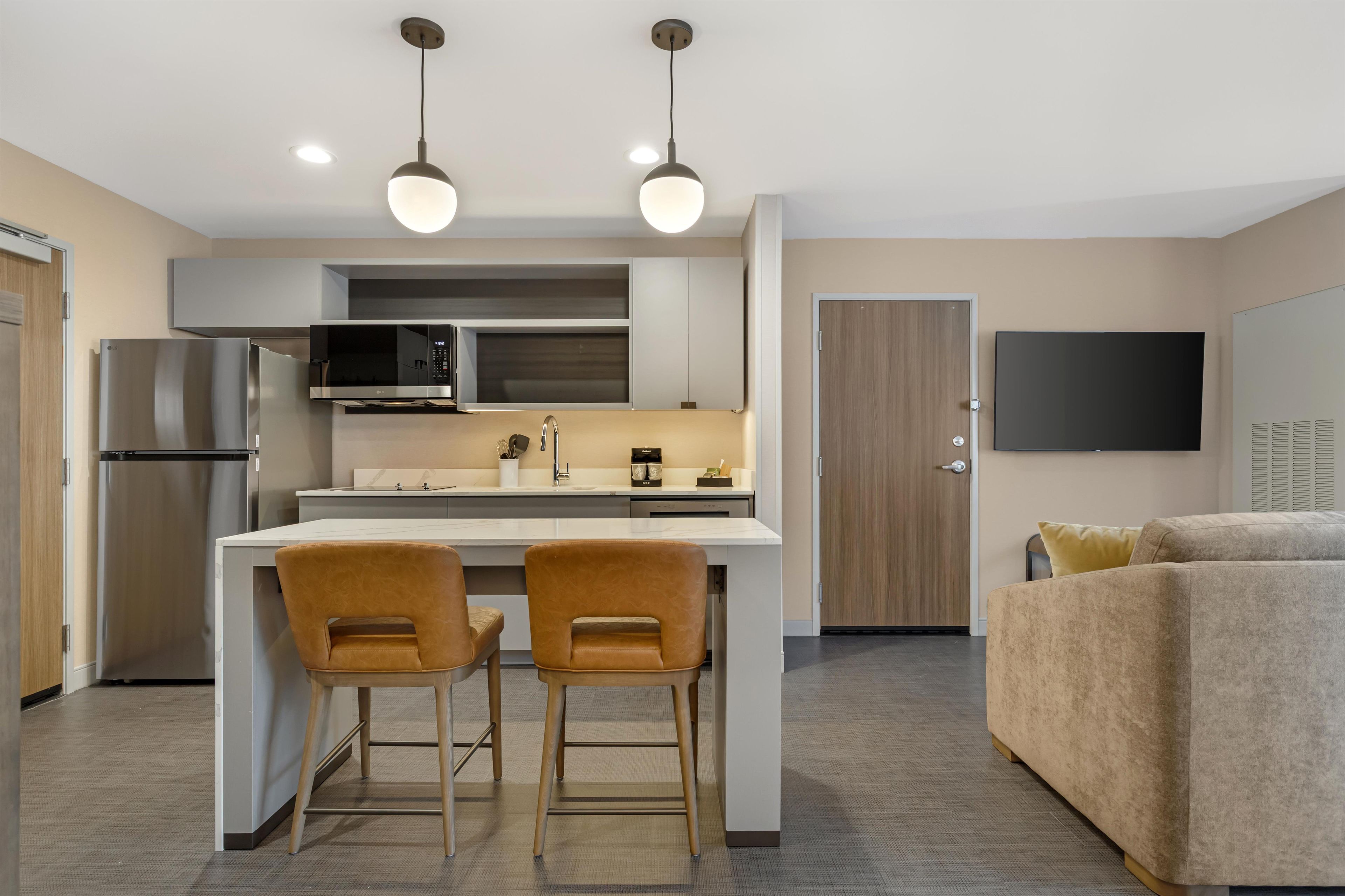 A modern kitchen with a central island, two bar stools, a built-in microwave, and a refrigerator.