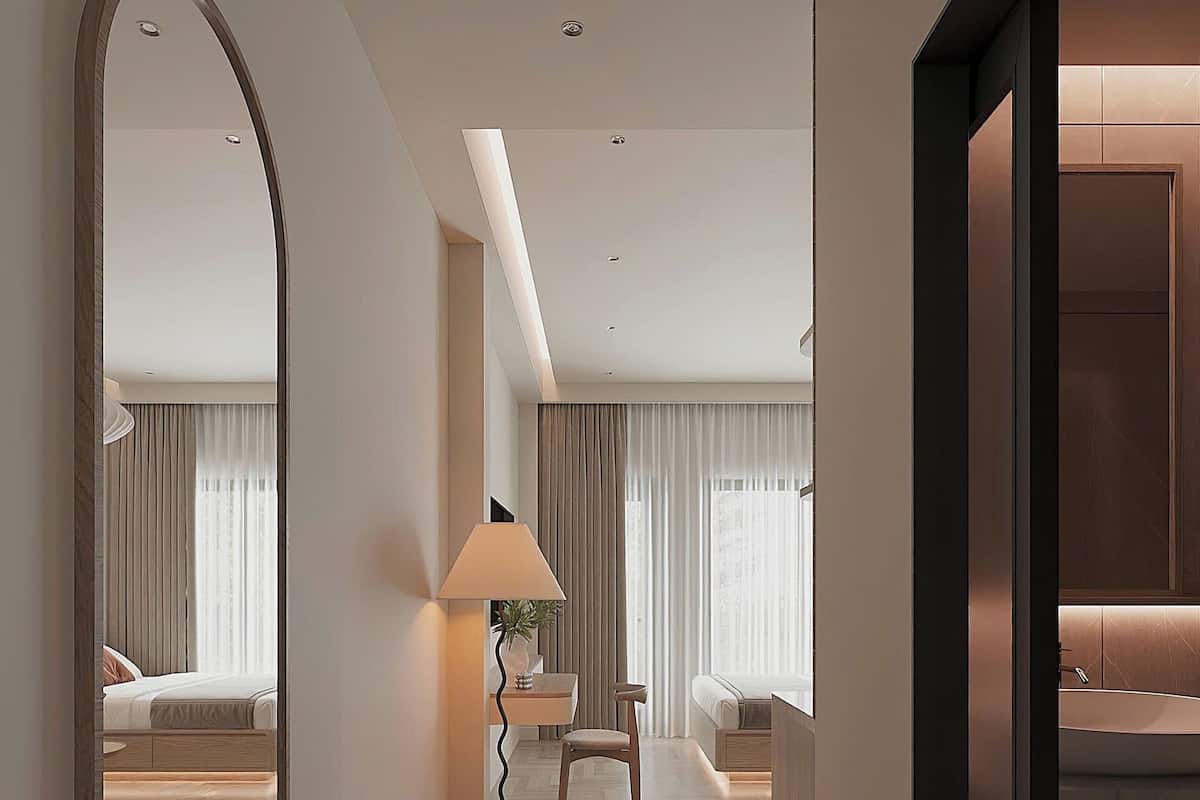 A modern hotel room with a large mirror, a bench, a desk, and a sofa.