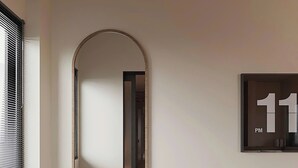 A modern bathroom with a bench, a round mirror, a clock, and a window with blinds. - Co Giang Premier Residence (Ho Chi Minh City)