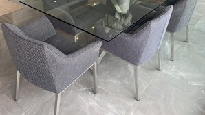 A modern dining area with a glass-top table, grey upholstered chairs, and a vase with white flowers. - Luxe 3-bedroom apartment on sea front in Cap-d'Ail with AC / Private pool (Cap-d'Ail)