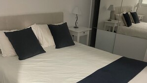 A neatly made bed with white and dark blue bedding, a bedside table with a lamp, and a mirror on the wall. - Luxe 3-bedroom apartment on sea front in Cap-d'Ail with AC / Private pool (Cap-d'Ail)