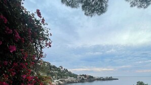 A patio with a view of the sea, a stone wall with flowers, and a tiled floor. - Luxe 3-bedroom apartment on sea front in Cap-d'Ail with AC / Private pool (Cap-d'Ail)