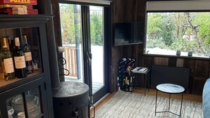 Un salon chaleureux avec un poêle à bois, une télévision et une vue sur la verdure environnante.