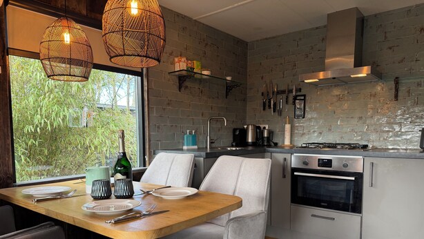 Une cuisine moderne avec un coin repas, comprenant une table en bois, des chaises grises et des luminaires suspendus en osier.