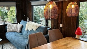 Une pièce chaleureuse avec un canapé, des fauteuils, une table en bois et deux lampes en osier suspendues au plafond.