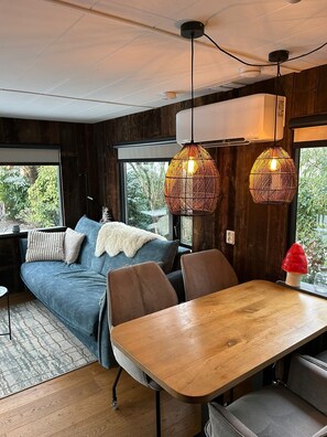 Ein gemütlicher Raum mit einer Couch, Sesseln, einem Holztisch und zwei hängenden Korbstühlen.