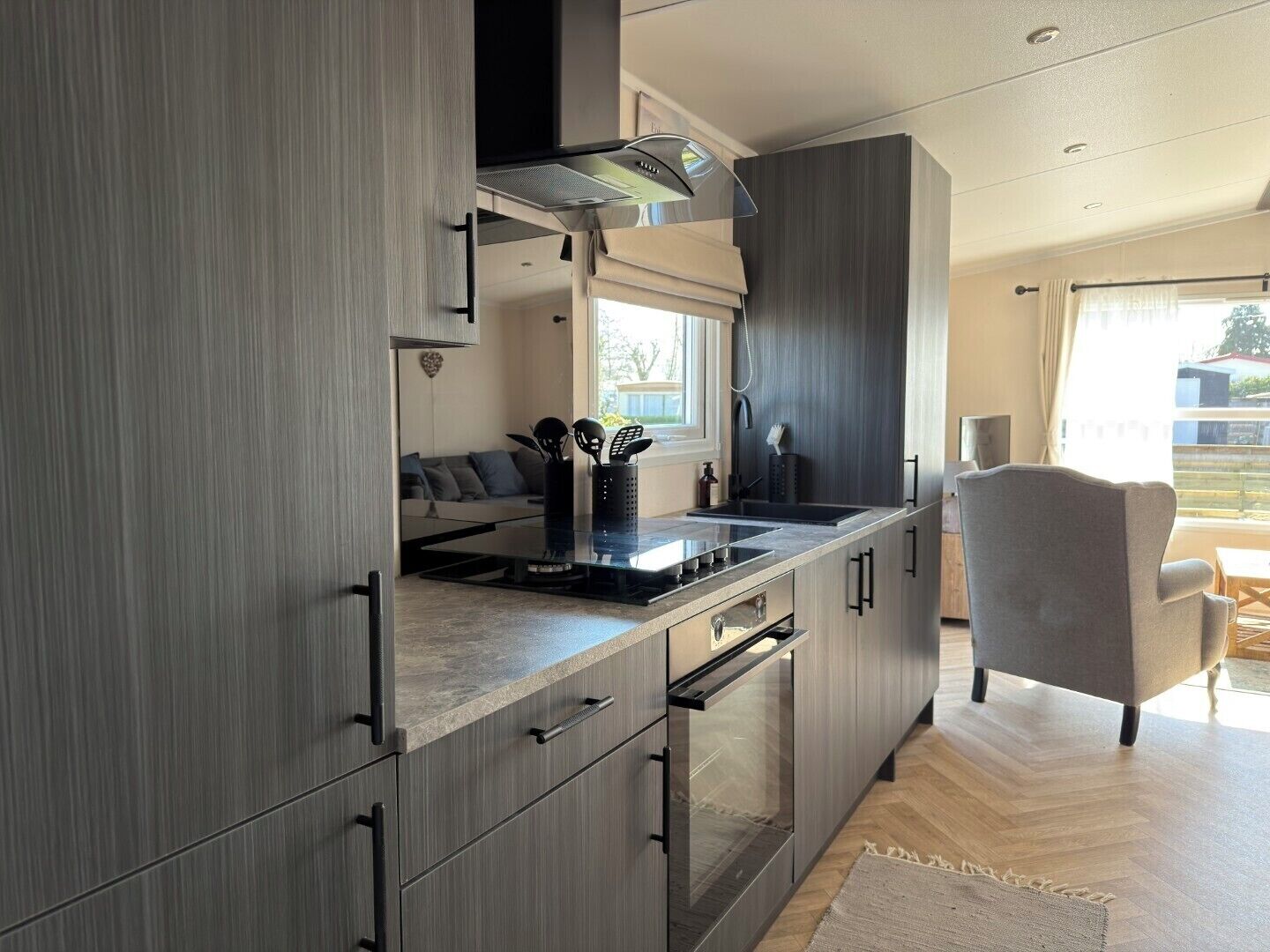 A modern kitchen with a built-in stove, oven, and microwave, a dining area with a gray chair, and a view of the outdoors.