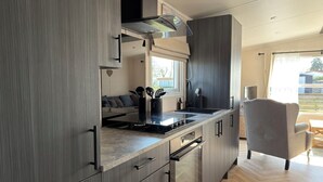 A modern kitchen with a built-in stove, oven, and microwave, a dining area with a gray chair, and a view of the outdoors. - Beautiful new chalet with private parking space on the edge of the park. (Sint Maarten)