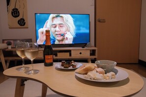 A table with a bottle of wine, glasses, a plate of food, and a bowl. A television is in the background. - Kaze Box/Seto Inland Sea/Families/Long stay/Kurashiki/Onomichi/Okayama (笠岡市)