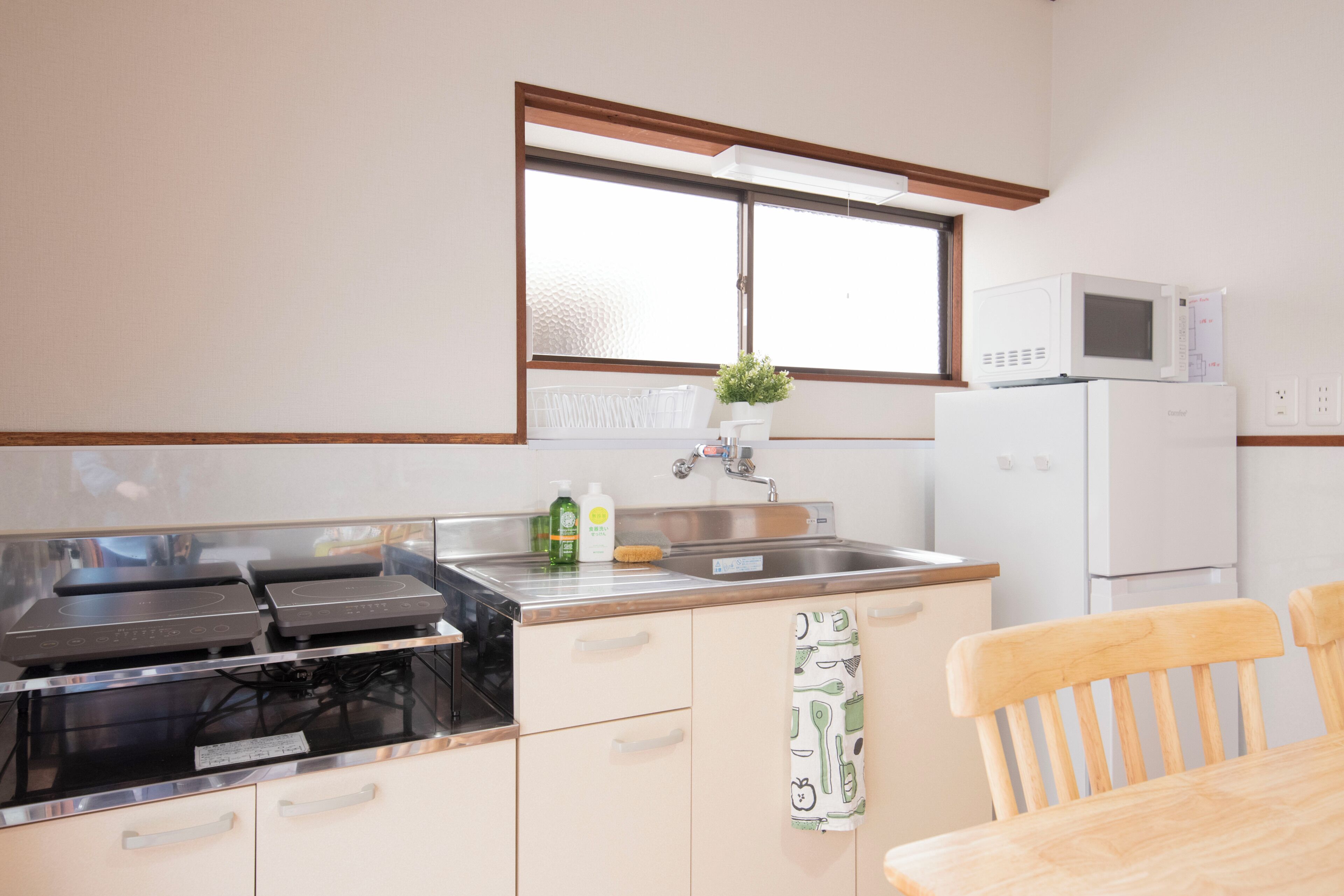 Una cocina con microondas, estufa, pileta y sillas de madera.