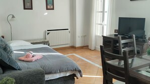 Quarto moderno com cama, mesa de cabeceira, luminária e uma TV sobre um suporte.