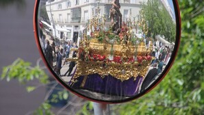 Espelho retrovisor refletindo um edifício com uma estátua e uma multidão.