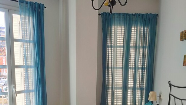Quarto com cama, cortinas, um lustre e vista pela janela.