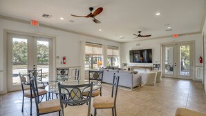 A spacious living area with a large TV, ceiling fans, and a dining area with chairs and a table. - Beach, Eats, Shops! Sunny Stay in our New 3BR Townhome in Peaceful Palm Coast FL (Palm Coast)