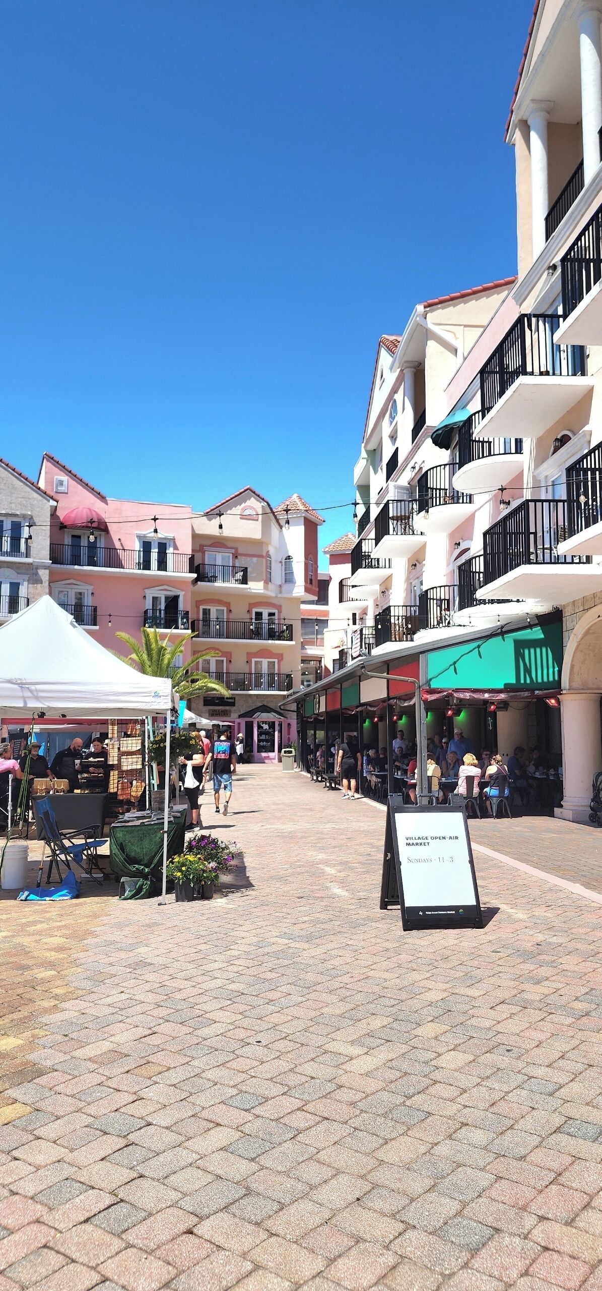 Zona peatonal con tiendas, un cartel y edificios con balcones.