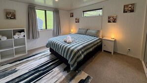 A bedroom with a bed, bedside tables, a window, a shelf with towels, and a rug. - Alpaca Farm Retreat - Peaceful Rural Escape (Lower Hutt)