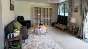 A living room with a sofa, armchairs, a coffee table, a TV, a bookshelf, and a window with curtains. - Alpaca Farm Retreat - Peaceful Rural Escape (Lower Hutt)