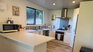 A modern kitchen with a large island, white cabinetry, a microwave, a stove, and a dishwasher. - Alpaca Farm Retreat - Peaceful Rural Escape (Lower Hutt)
