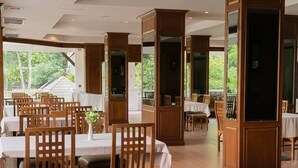 A restaurant with wooden chairs and tables, large wooden pillars, and a view of greenery outside. - Lanna Oriental Maejo (San Sai)