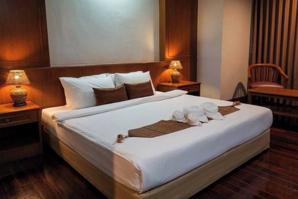 Una habitación de hotel con una cama grande, dos lámparas de noche, un cabecero de madera, una silla y un ventanal con cortinas.